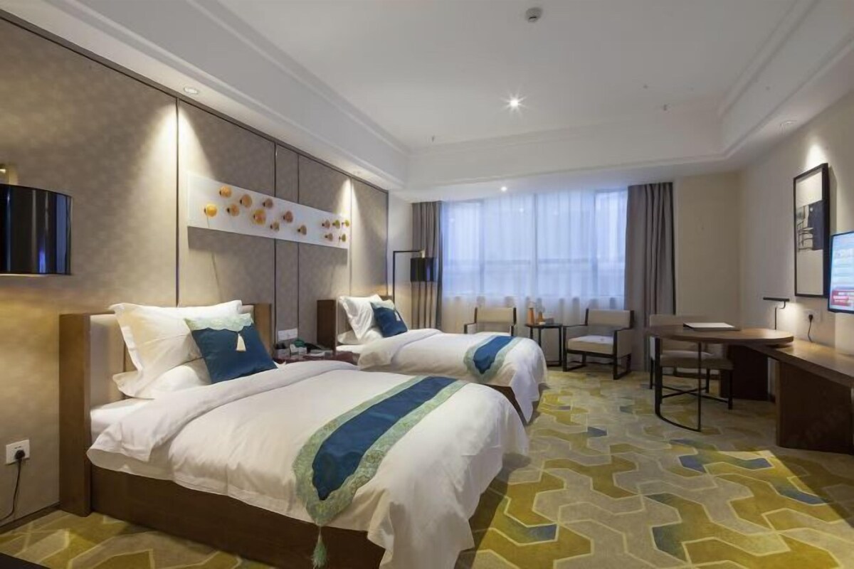 A hotel room with two beds, a desk, a chair, a TV, and a window with curtains.