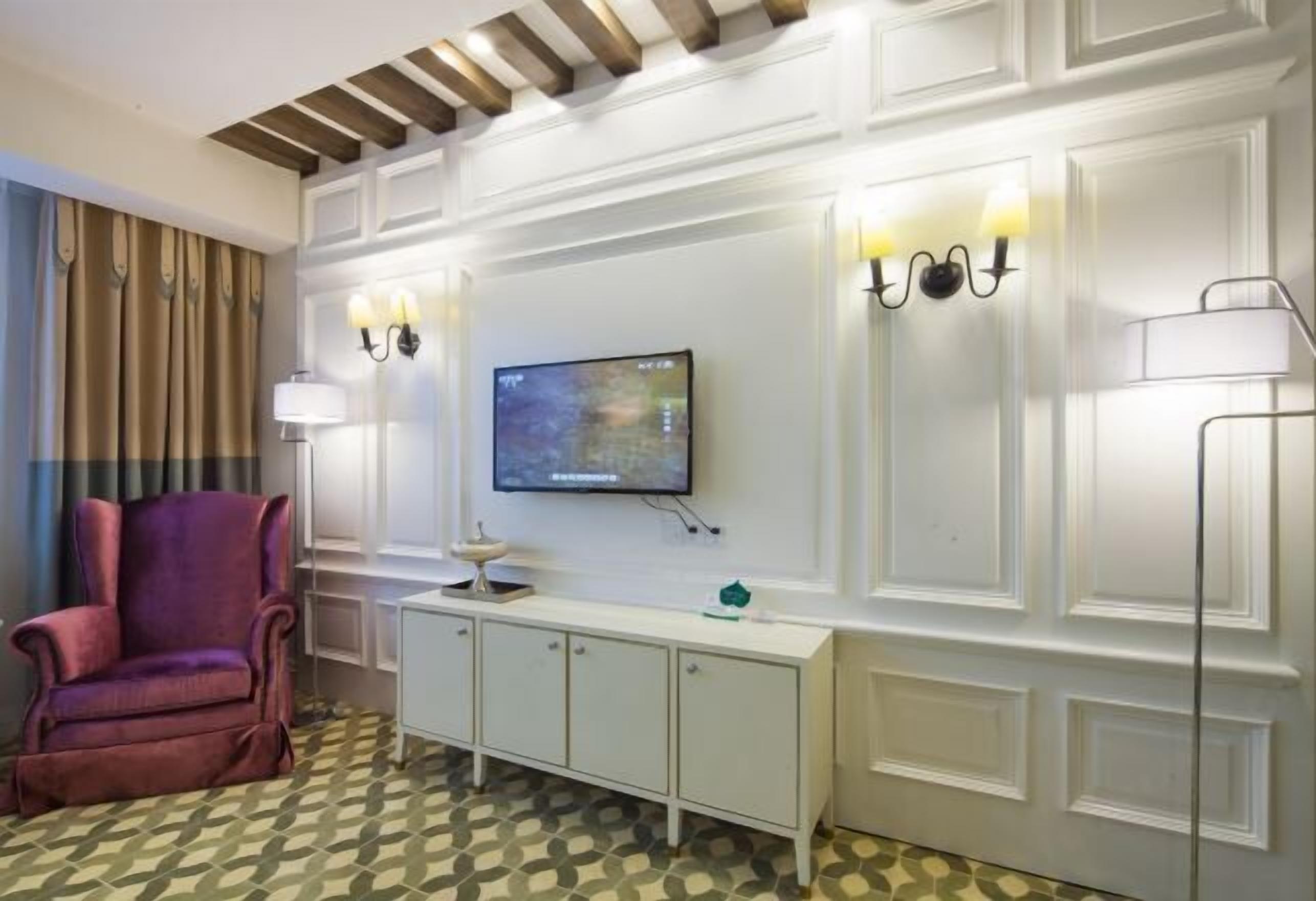Ein Hotelzimmer mit Fernseher, einem gepolsterten Sessel, einem weißen Konsolentisch und gefliestem Boden mit Muster.