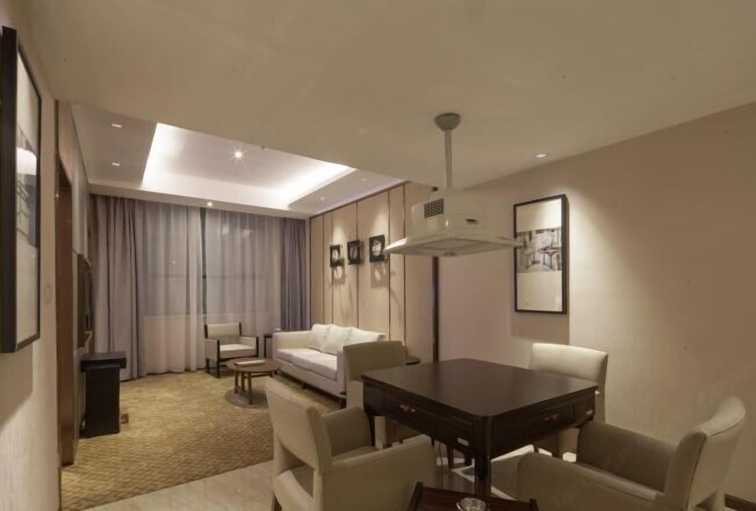 A modern hotel room with a dining area, a sofa, a small table, and a ceiling light.
