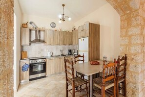 Een keuken met houten kasten, een fornuis, een koelkast en een eettafel met stoelen.