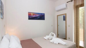 A hotel room with a bed, a painting of a sunset, an air conditioning unit, and a mirror. - Selinitsa Stone Residence-Private Poolside Retreat (Agios Nikolaos)