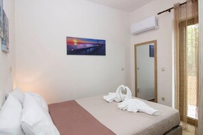 A hotel room with a bed, a painting of a sunset, an air conditioning unit, and a mirror. - Selinitsa Stone Residence-Private Poolside Retreat (Agios Nikolaos)