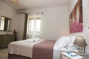 A neatly arranged bedroom with a bed, bedside table, lamp, and a painting on the wall.