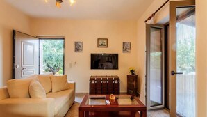A living room with a sofa, a coffee table, a television, and a sliding glass door. - Selinitsa Stone Residence-Private Poolside Retreat (Agios Nikolaos)