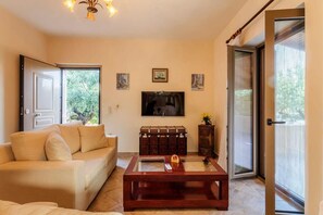 A living room with a sofa, a coffee table, a television, and a sliding glass door. - Selinitsa Stone Residence-Private Poolside Retreat (Agios Nikolaos)