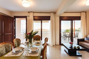 A dining area with a table set for four, chairs, a coffee table, and a view of the sea through large windows.