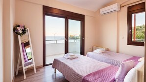 A bedroom with two beds, a balcony with a view, and an air conditioning unit. - Armonia by the Sea - Majestic Seaside Retreat (Petalidi)