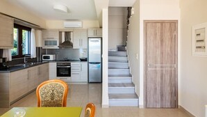 A modern kitchen with a dining area, a staircase, and a wooden door. - Armonia by the Sea - Majestic Seaside Retreat (Petalidi)