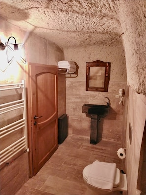 A small, rustic bathroom with a wooden door, a sink, a toilet, and a mirror. - Cappadocia Alaz Cave Otel (Nevsehir)
