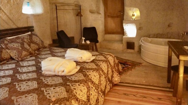 A cozy bedroom with a bed, two chairs, a small table, a bathtub, and a door. - Cappadocia Alaz Cave Otel (Nevsehir)