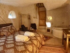 A cozy bedroom with a bed, two chairs, a small table, a bathtub, and a door. - Cappadocia Alaz Cave Otel (Nevsehir)