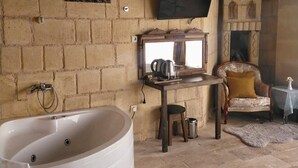 A rustic room with a large bathtub, a television mounted on the wall, a fireplace, and a vintage armchair. - Cappadocia Alaz Cave Otel (Nevsehir)