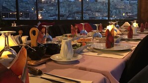 A dining table set with plates, cutlery, and a candle, overlooking a cityscape at dusk. - Cappadocia Alaz Cave Otel (Nevsehir)