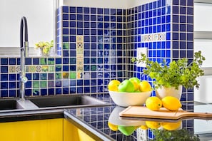 A kitchen with a sink, a bowl of fruit, a potted plant, and a cutting board. - Manella On Kloof (Cape Town)
