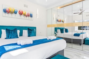 Une chambre d’hôtel moderne avec un grand lit, une cloison en verre et une œuvre d’art colorée au-dessus du lit.
