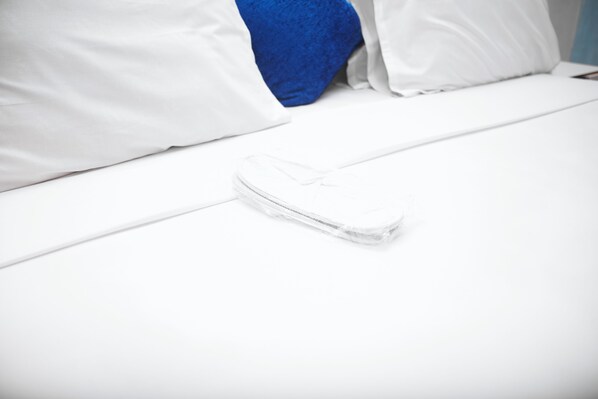 Una cama bien hecha con ropa blanca y un solo zapato blanco sobre ella.