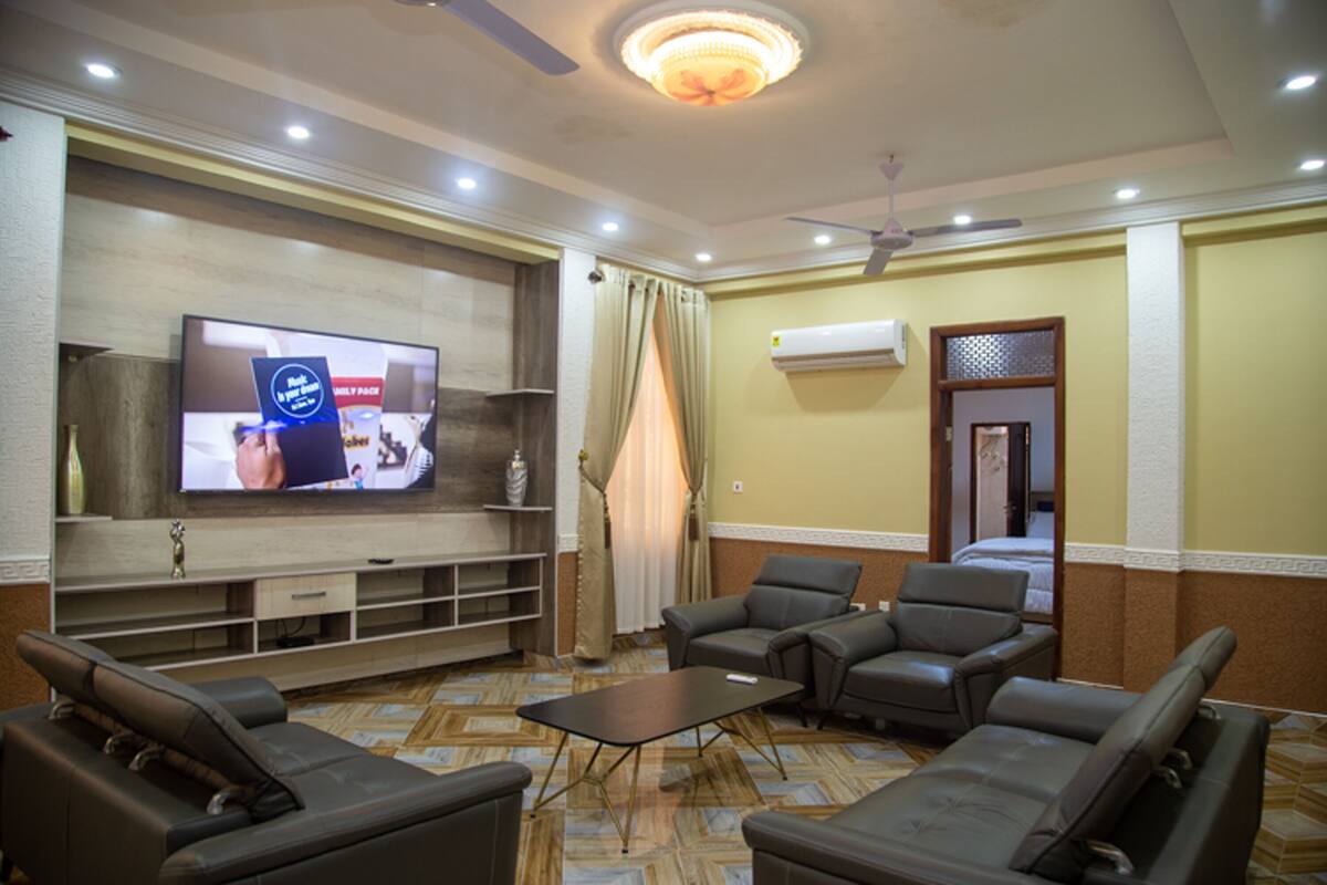 Habitación de hotel con televisor de pantalla plana en la pared, ventilador de techo, sofá y mesa de centro.