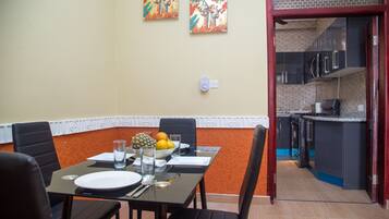 A dining area with a table set for four, a fruit bowl, and two wall-mounted paintings.