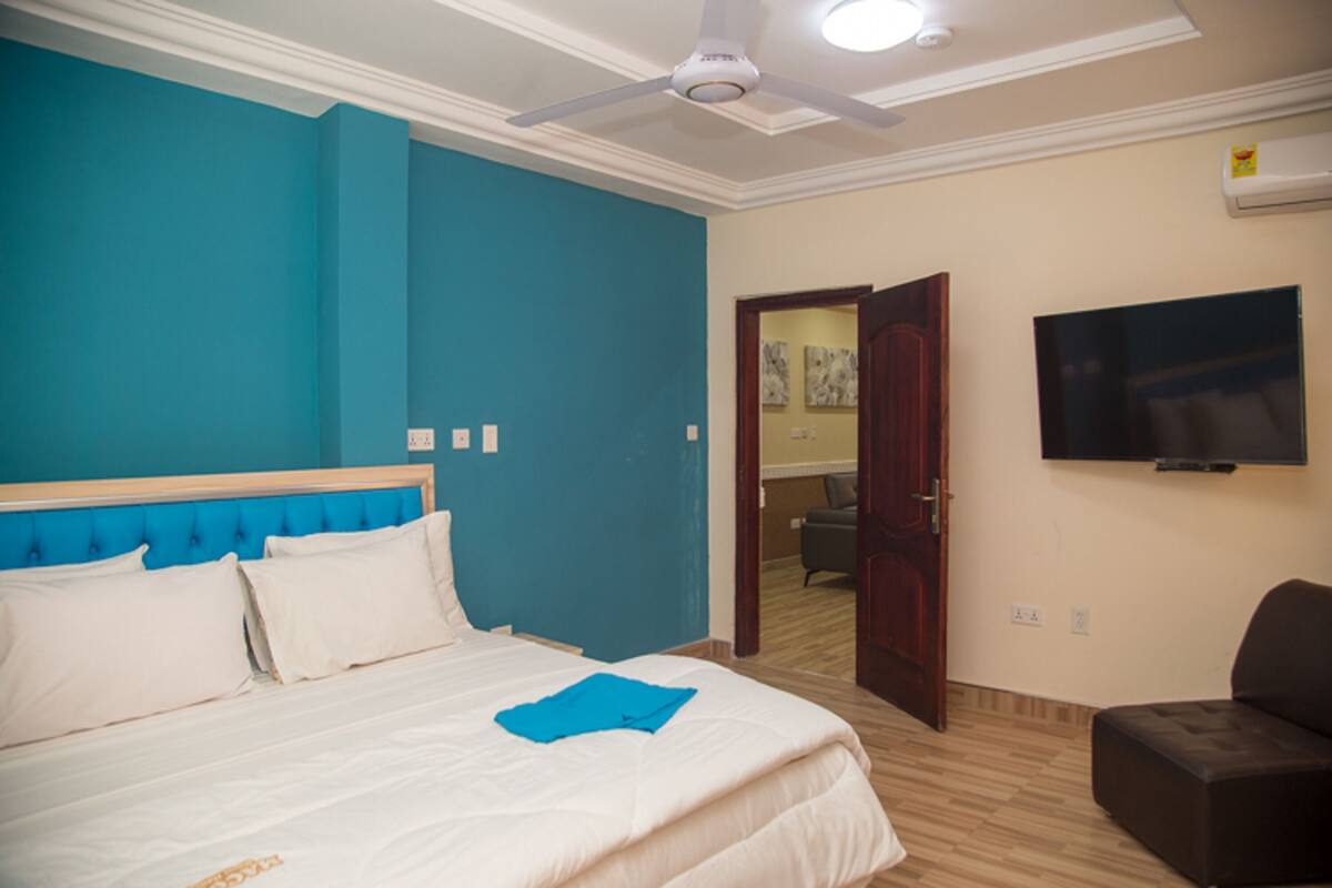 Habitación de hotel con cama, ventilador de techo, televisión y puerta que da a otra habitación.