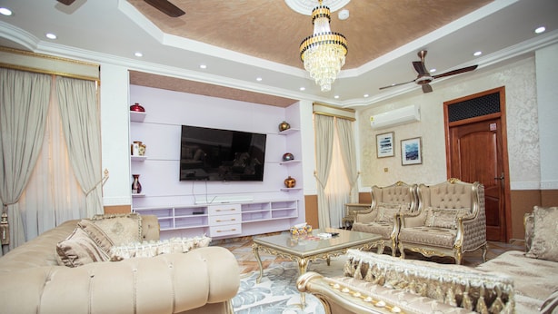 Un salon luxueux doté d’un grand téléviseur à écran plat, de canapés moelleux, d’un lustre et d’un ventilateur de plafond.