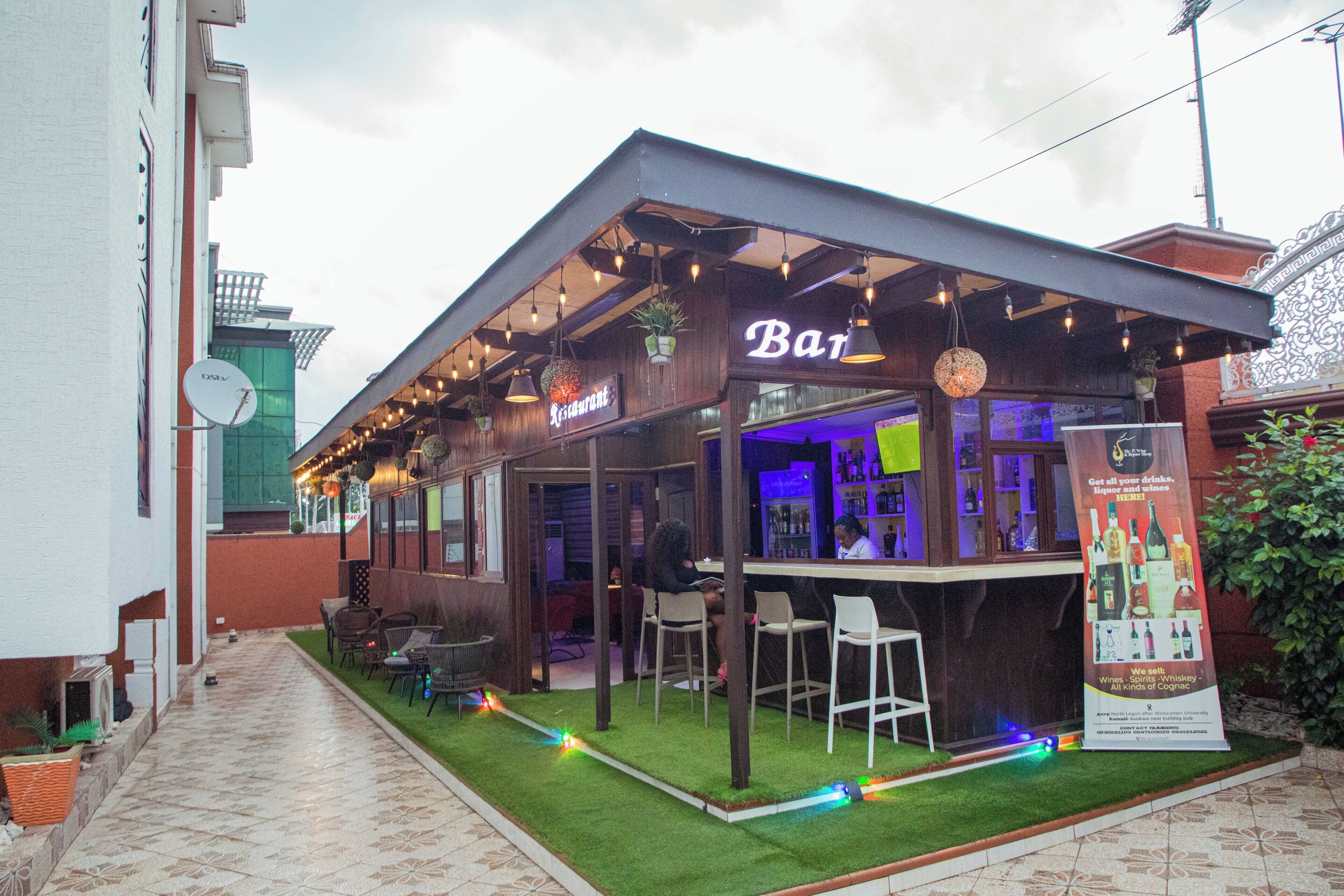Een openluchtcafé met een overdekte zithoek, een bar en een bord waarop staat dat het een restaurant is.