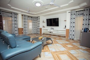 Una sala de estar con un sofá azul, una mesa de centro de cristal, un televisor de pantalla plana y cortinas con estampado.
