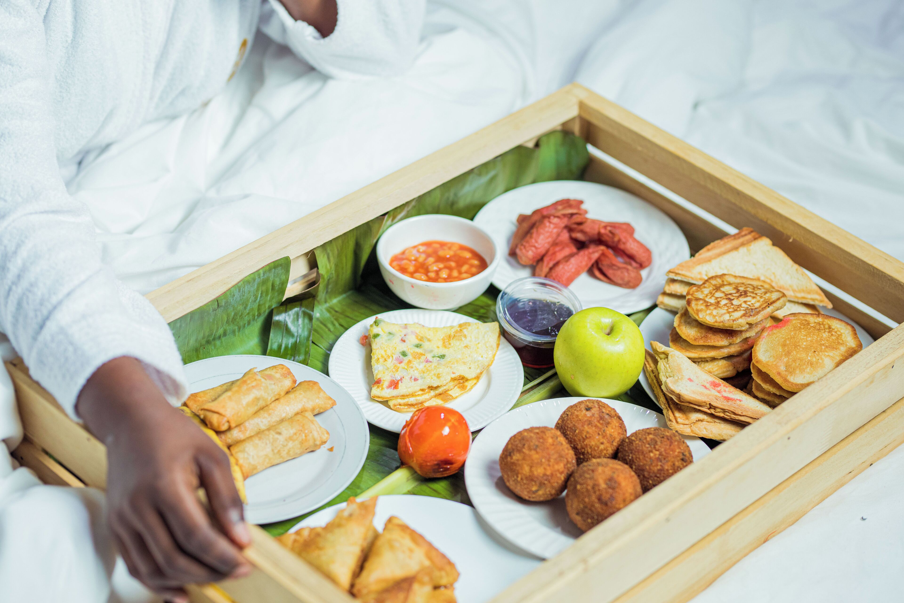A tray of food including sandwiches, omelets, and various snacks on a bed.