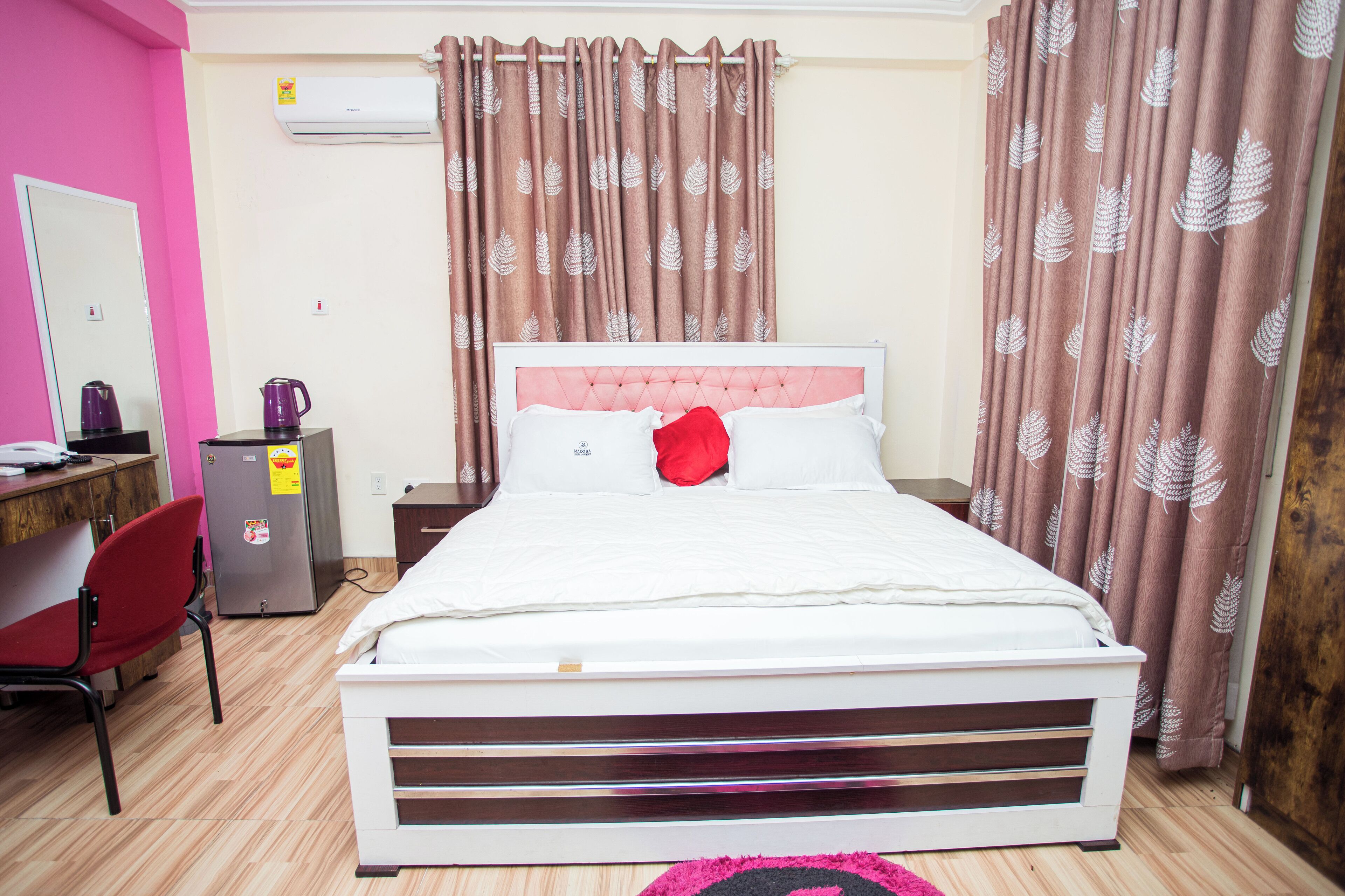 Een slaapkamer met een bed, bureau, stoel, airconditioning en gordijnen.