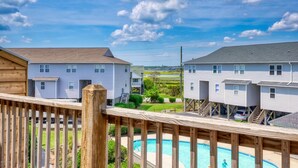 Ein Wohngebiet mit einer Holzterrasse mit Blick auf einen Swimmingpool, umgeben von Häusern und einem klaren Himmel.