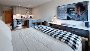 Een moderne hotelkamer met een groot bed, een bureau met een computer, een televisie en een kitchenette.