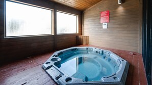 Een hottub in een houten kamer met grote ramen en een houten plafond.