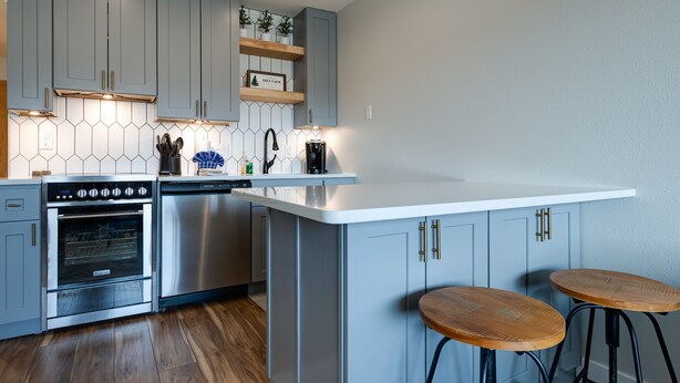 Een moderne keuken met grijze kastjes, een wit aanrecht en twee houten stoelen.