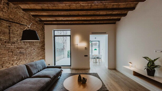 A modern living room with a brick wall, a wooden ceiling, a grey sofa, a round coffee table, and a view into another room with a dining area. - Petit Luxe Sant Pere (Terrassa)