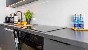 A modern kitchen with a dishwasher, a coffee maker, a plant, and two bottles of Perrier water on the counter.