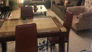 A living room with a dining table, chairs, sofas, a chandelier, and a painting on the wall. - Stay.Plus Kahawa Sukari Apartment (Ruiru)