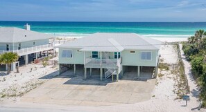 Een huis aan het strand met een balkon, een overdekte veranda en een oprit van zand.