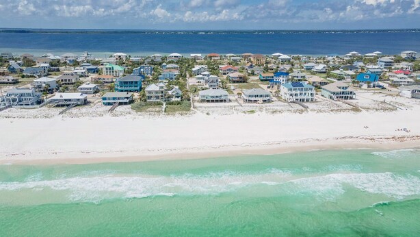 Vista aérea de una zona residencial costera con casas a lo largo de la playa, una playa de arena y el océano.