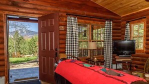 A log cabin room with a bed, a television, and a view of a mountainous landscape. - The Log Cabin at PeaceRidge (Wilmington)