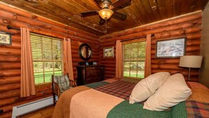 A log cabin bedroom with a bed, a chair, a dresser, and a ceiling fan. - The Log Cabin at PeaceRidge (Wilmington)