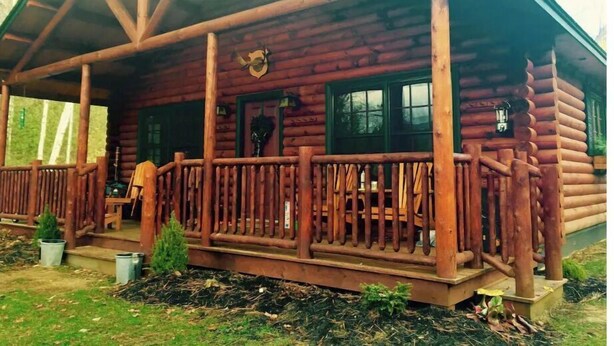 A log cabin with a porch, a small garden, and a visible door. - The Log Cabin at PeaceRidge (Wilmington)