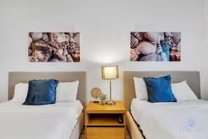 A hotel room with two beds, a nightstand with a lamp, and wall art.