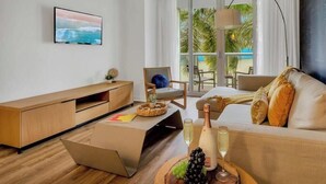 A modern hotel room with a large window, a flat-screen TV, a sofa, a chair, and a lamp.