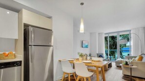 Une cuisine moderne dotée d’un réfrigérateur encastré, d’un coin repas avec des chaises et une table, d’un canapé et d’une grande fenêtre offrant une vue sur la verdure.