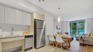 A modern kitchen with white cabinets, a stainless steel refrigerator, and a dining area with a table and chairs.