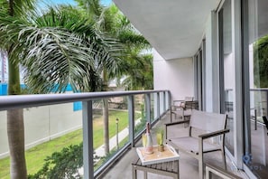 Relax on the balcony with a table and chairs, taking in the serene views of the well-maintained lawn and palm tree.