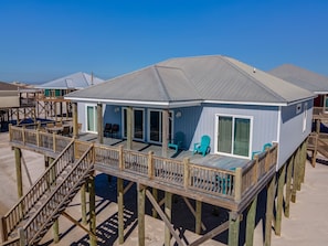 A beach house with a deck, outdoor seating, and a staircase leading to the upper level. - Awake On The Gulf - Gulf Front! Gaze Up At The Stars From Your Large Deck While Listening To The Waves Crash. 4 Bedroom Home by RedAwning (Dauphin Island)