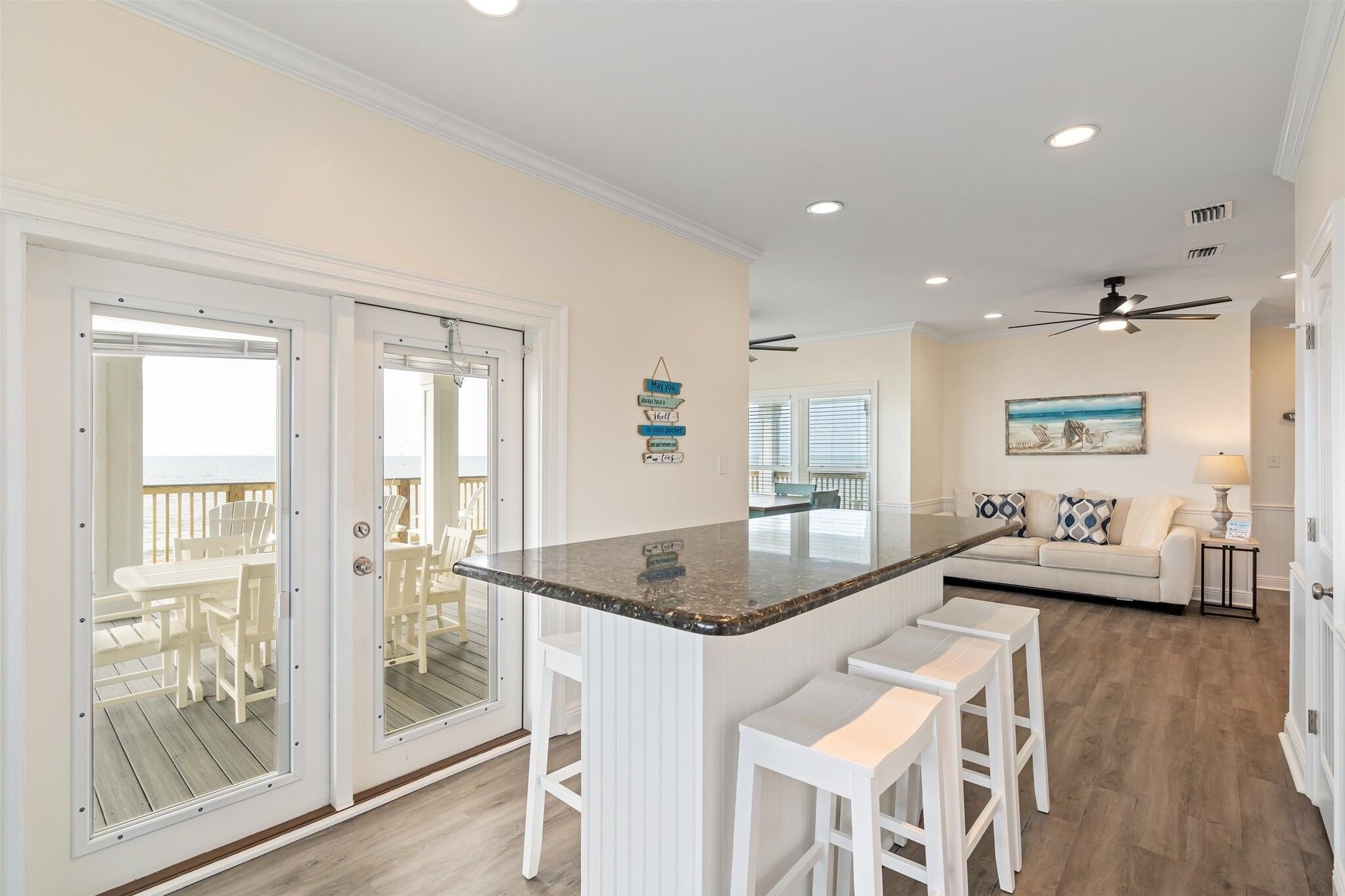 A modern kitchen with a central island, white bar stools, and a view to an outdoor deck.