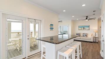 A modern kitchen with a central island, white bar stools, and a view to an outdoor deck.