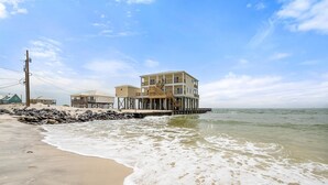 A beachfront property with a multi-level building on stilts, a sandy beach, and a clear sky. - Shamrock Shores - Gulf Front West End Pet Friendly Property With Room For Everyone. 3 Master Suites! 6 Bedroom Home by RedAwning (Dauphin Island)