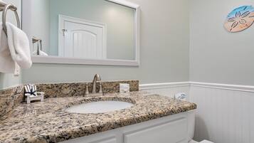 A bathroom with a granite countertop sink, a white vanity, a towel rack, and a decorative wall piece.
